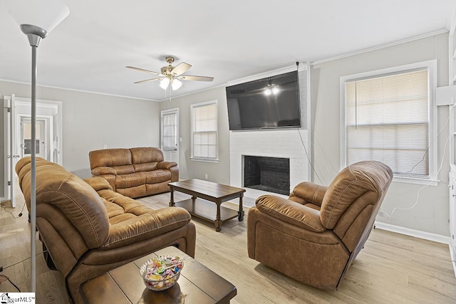 living room featuring ceiling fan, light wood-type flooring, ornamental molding, and a brick fireplace