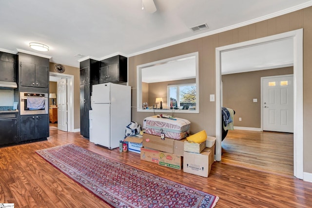 kitchen with oven, white refrigerator, wood-type flooring, and crown molding