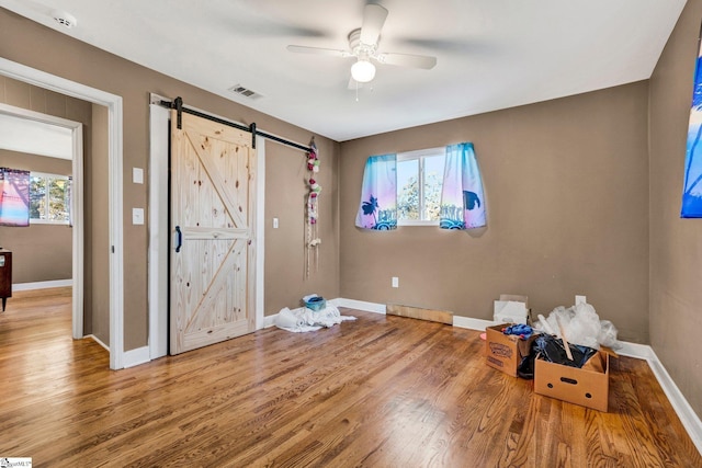 unfurnished bedroom featuring wood-type flooring, a barn door, and ceiling fan