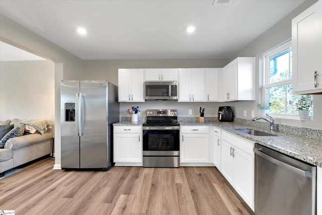 kitchen with white cabinets, sink, light wood-type flooring, light stone counters, and stainless steel appliances