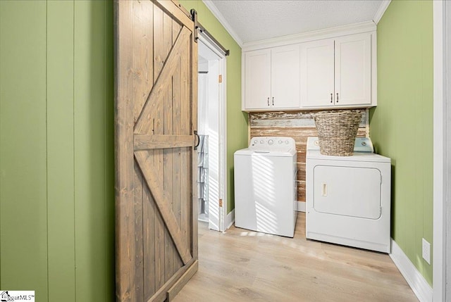 laundry room featuring cabinets, a barn door, crown molding, light hardwood / wood-style floors, and washer and clothes dryer