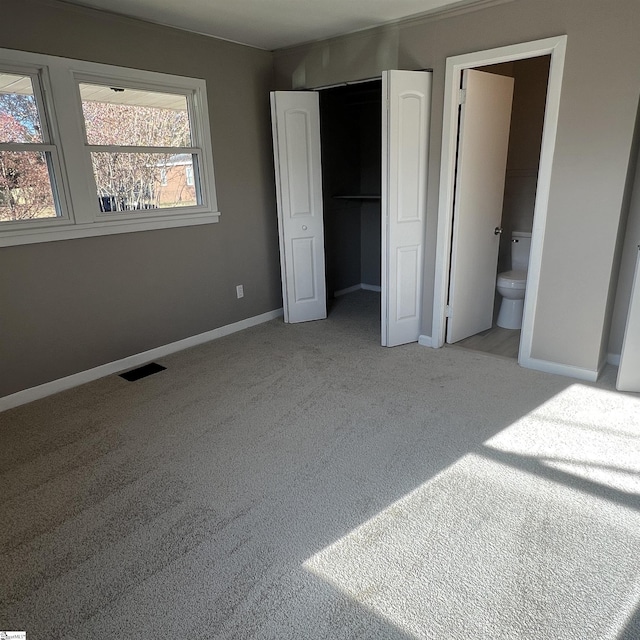 unfurnished bedroom with light carpet, ensuite bathroom, and a closet