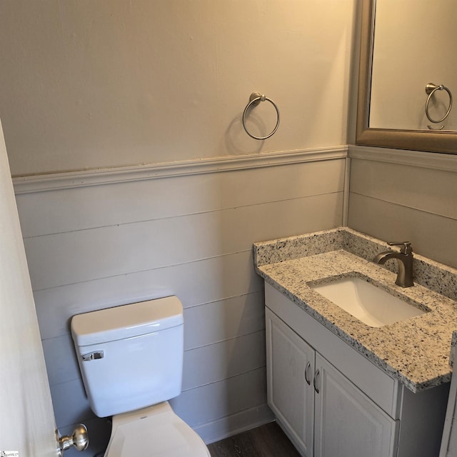 bathroom featuring hardwood / wood-style flooring, vanity, toilet, and wooden walls