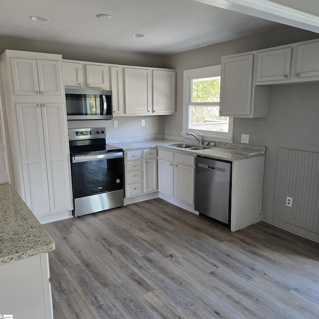 kitchen with appliances with stainless steel finishes, light stone counters, sink, light hardwood / wood-style floors, and white cabinetry