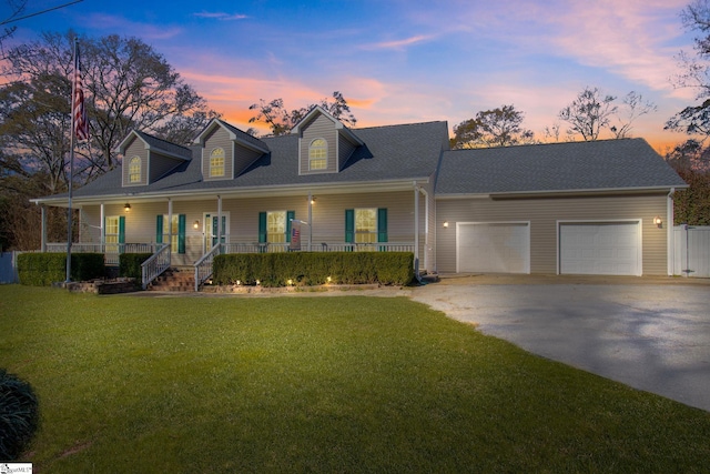 cape cod house featuring covered porch, a yard, and a garage