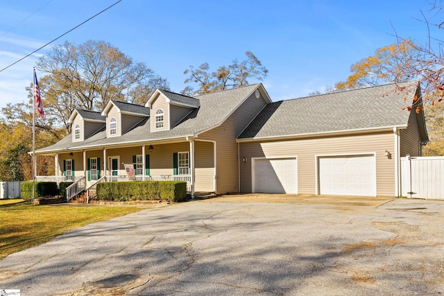 new england style home featuring a porch, a garage, and a front yard