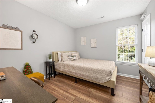 bedroom with hardwood / wood-style floors, a textured ceiling, and multiple windows