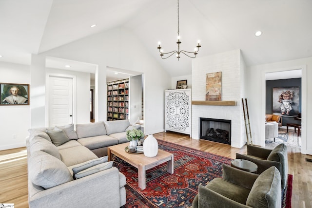 living room featuring a chandelier, wood-type flooring, a large fireplace, and high vaulted ceiling