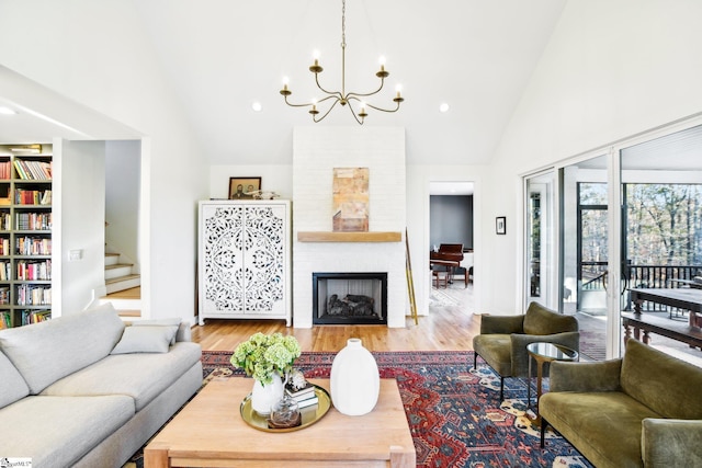 living room with a large fireplace, high vaulted ceiling, light hardwood / wood-style floors, and an inviting chandelier