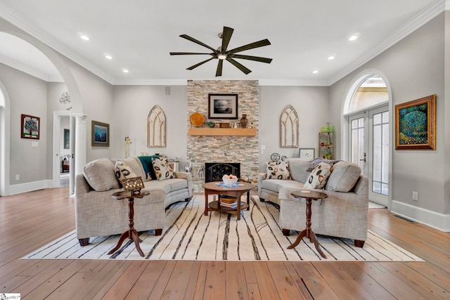 living room with a stone fireplace, a wealth of natural light, ornamental molding, and light wood-type flooring