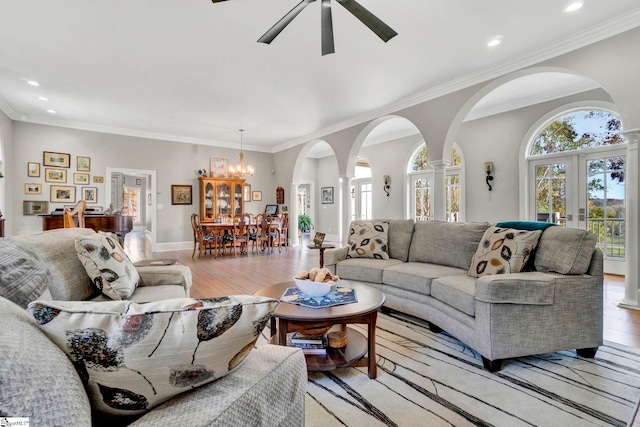 living room featuring ceiling fan with notable chandelier, light wood-type flooring, crown molding, and french doors