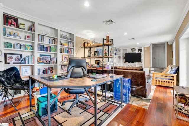 home office with wood-type flooring, built in shelves, and ornamental molding