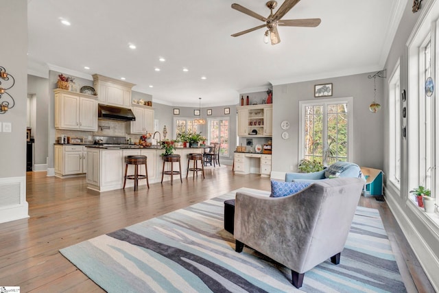 living room with ceiling fan, crown molding, and light wood-type flooring