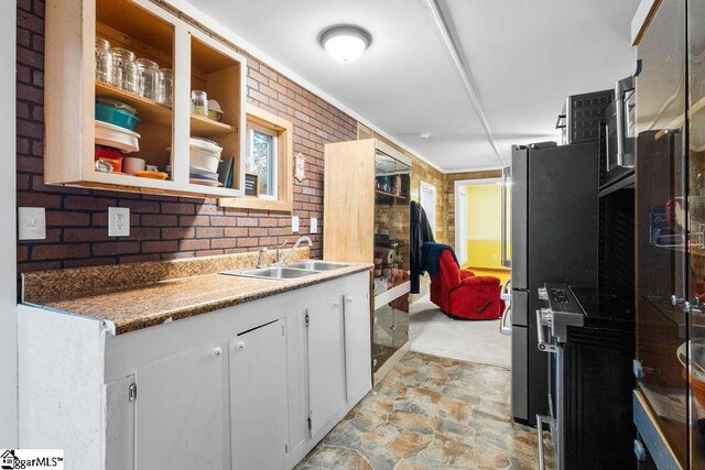 kitchen with stainless steel fridge, white cabinetry, sink, and brick wall