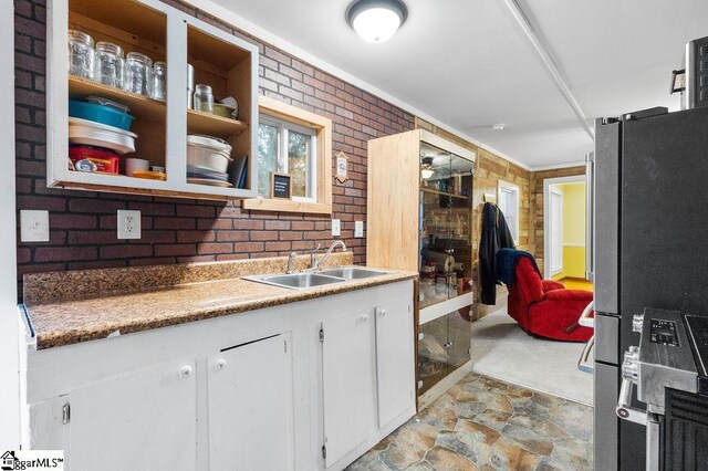 kitchen with white cabinets, stainless steel fridge, sink, and brick wall