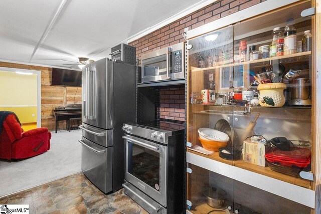 kitchen featuring ceiling fan, stainless steel appliances, brick wall, carpet floors, and wooden walls