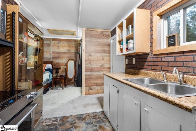 kitchen featuring sink, dark colored carpet, brick wall, wood walls, and electric stove