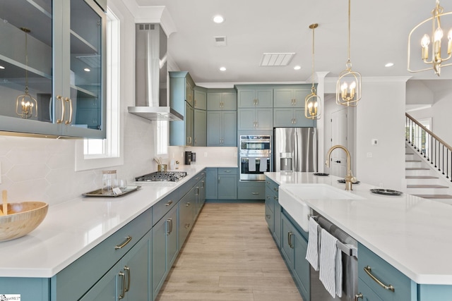 kitchen featuring sink, wall chimney exhaust hood, stainless steel appliances, light hardwood / wood-style flooring, and decorative light fixtures