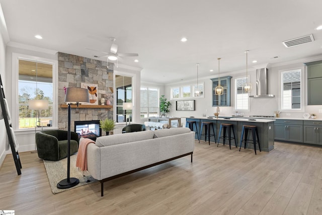 living room featuring ceiling fan with notable chandelier, light hardwood / wood-style floors, plenty of natural light, and crown molding