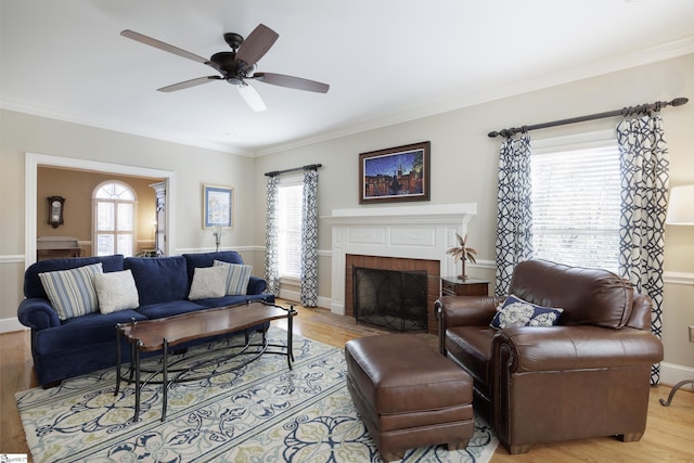 living room with ceiling fan, light hardwood / wood-style floors, ornamental molding, and a brick fireplace