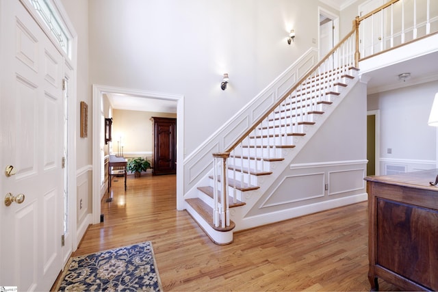 entrance foyer with crown molding, light hardwood / wood-style flooring, and a towering ceiling