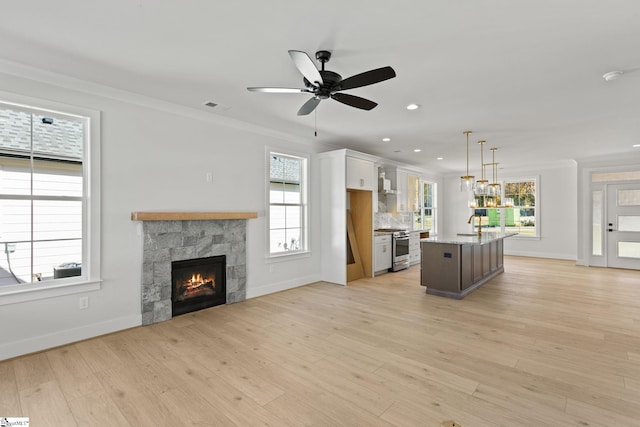 kitchen with white cabinetry, a kitchen island with sink, hanging light fixtures, and light hardwood / wood-style flooring