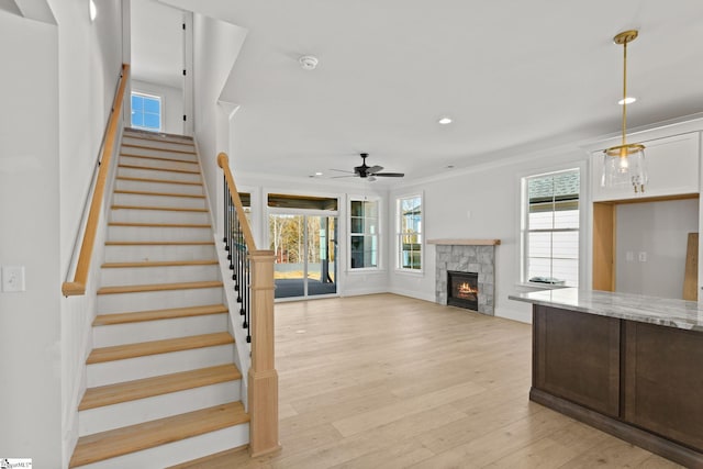 stairs featuring hardwood / wood-style floors, ceiling fan, a stone fireplace, and crown molding