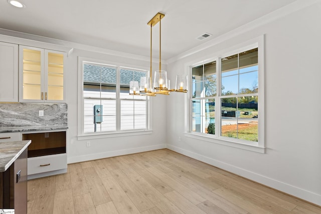 unfurnished dining area featuring a chandelier, crown molding, and light hardwood / wood-style floors