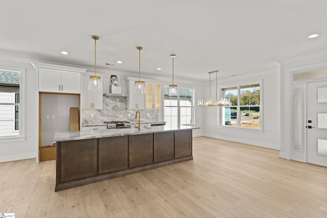 kitchen with light stone countertops, light wood-type flooring, crown molding, white cabinets, and hanging light fixtures