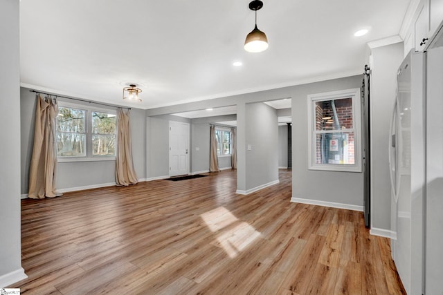 unfurnished living room with a barn door, light hardwood / wood-style floors, and crown molding