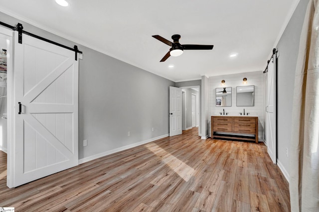 unfurnished bedroom with ceiling fan, a barn door, light hardwood / wood-style floors, and ornamental molding