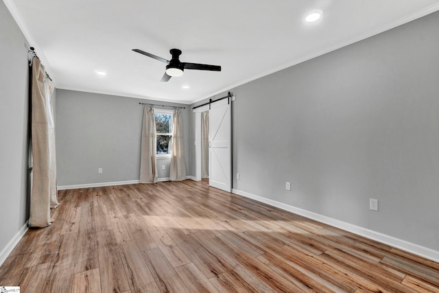 unfurnished bedroom featuring ceiling fan, a barn door, light wood-type flooring, and crown molding