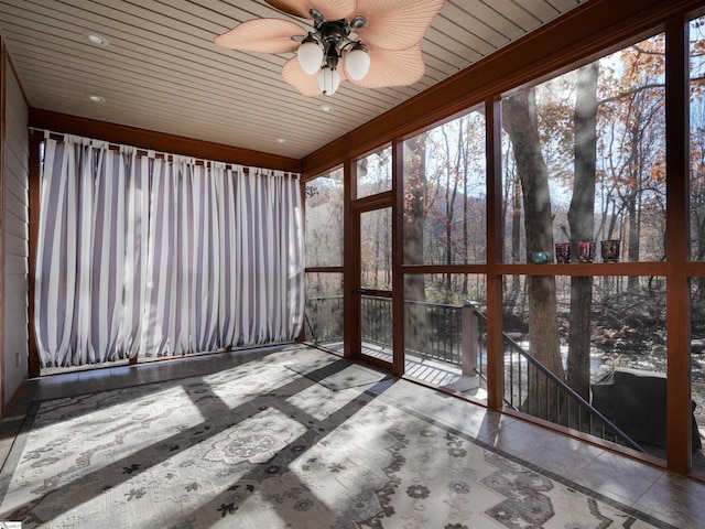 unfurnished sunroom with ceiling fan, a healthy amount of sunlight, and wood ceiling