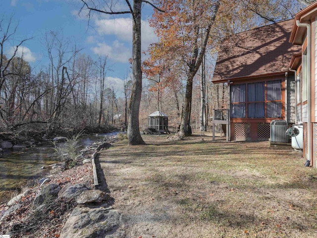 view of yard with central AC unit, a sunroom, and a water view