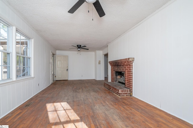 unfurnished living room featuring a textured ceiling, ceiling fan, dark wood-type flooring, and a brick fireplace