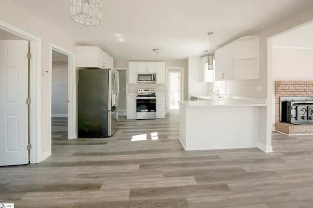 kitchen with appliances with stainless steel finishes, sink, pendant lighting, white cabinets, and light hardwood / wood-style floors