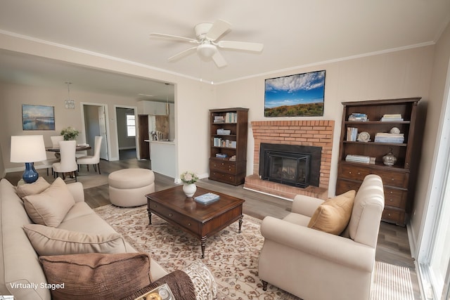 living room with light hardwood / wood-style floors, a brick fireplace, ceiling fan, and ornamental molding