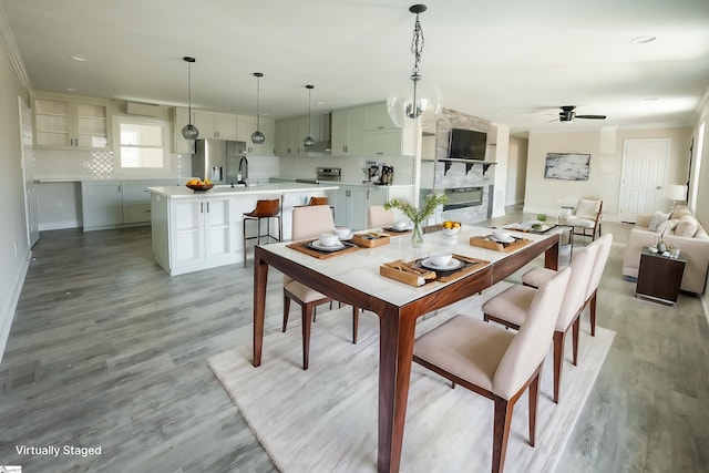 dining room with ceiling fan with notable chandelier, crown molding, sink, a fireplace, and light hardwood / wood-style floors