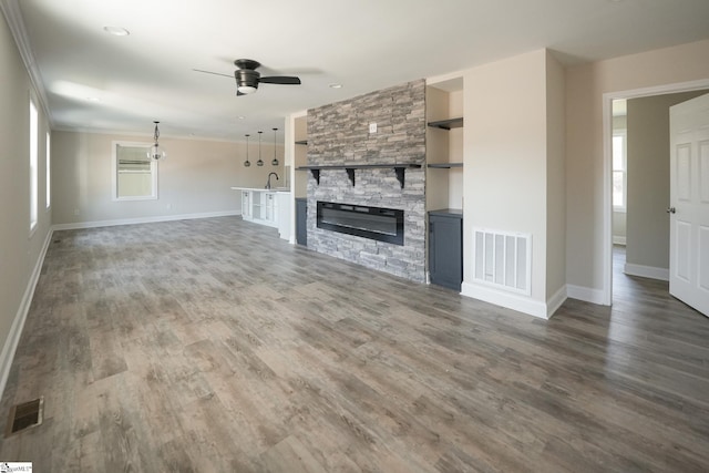 unfurnished living room featuring a stone fireplace, ceiling fan, dark wood-type flooring, and sink