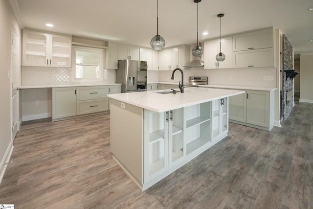 kitchen featuring appliances with stainless steel finishes, a kitchen island with sink, wall chimney range hood, sink, and wood-type flooring