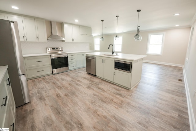 kitchen featuring a center island with sink, sink, wall chimney exhaust hood, decorative light fixtures, and stainless steel appliances