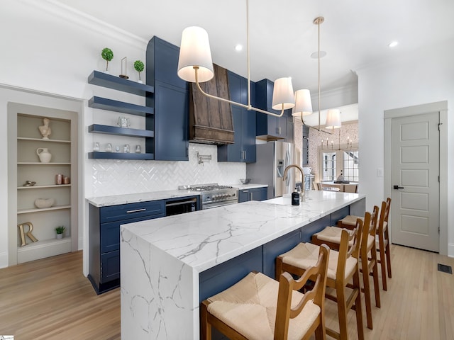 kitchen with blue cabinetry, light stone countertops, hanging light fixtures, light hardwood / wood-style flooring, and a breakfast bar area