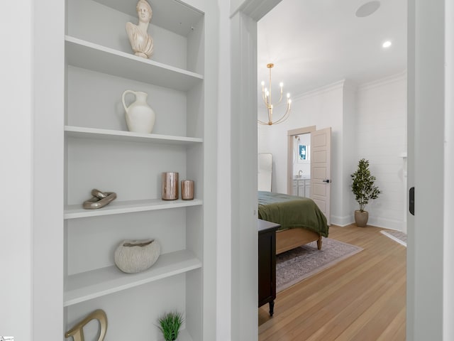 hall with built in shelves, crown molding, light hardwood / wood-style floors, and a notable chandelier