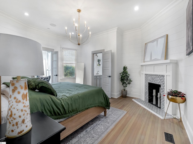 bedroom featuring crown molding, a fireplace, light hardwood / wood-style floors, and an inviting chandelier