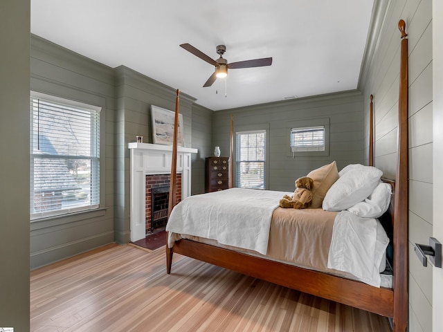 bedroom with ceiling fan, light hardwood / wood-style floors, a fireplace, and multiple windows