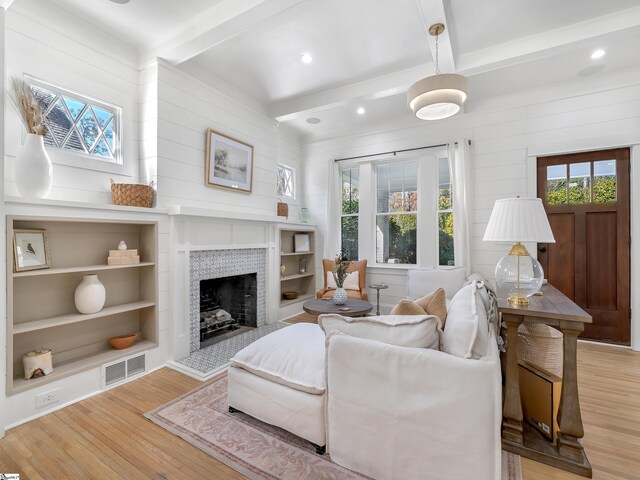 living room featuring beam ceiling, a tiled fireplace, and light hardwood / wood-style flooring