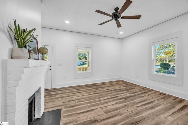 unfurnished living room featuring wood-type flooring, a brick fireplace, ceiling fan, and a healthy amount of sunlight