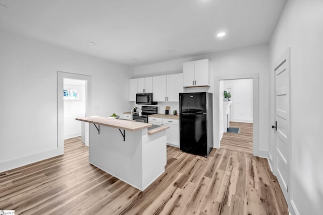 kitchen featuring a kitchen bar, a kitchen island with sink, black appliances, light hardwood / wood-style flooring, and white cabinetry