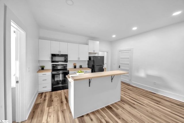 kitchen with a breakfast bar, wooden counters, black appliances, white cabinets, and light wood-type flooring