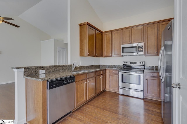 kitchen featuring kitchen peninsula, dark stone countertops, vaulted ceiling, appliances with stainless steel finishes, and hardwood / wood-style flooring